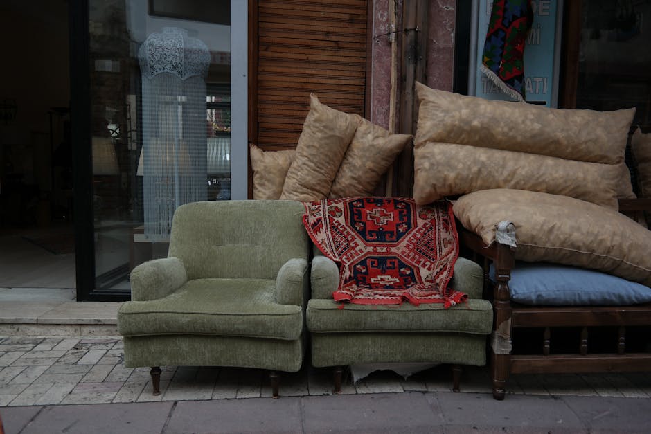 An abandoned, dirty upholstered sofa with torn and stained fabric, positioned against a graffiti-covered brick wall in a dimly lit, neglected urban alleyway. The sofa appears weathered and dusty, with